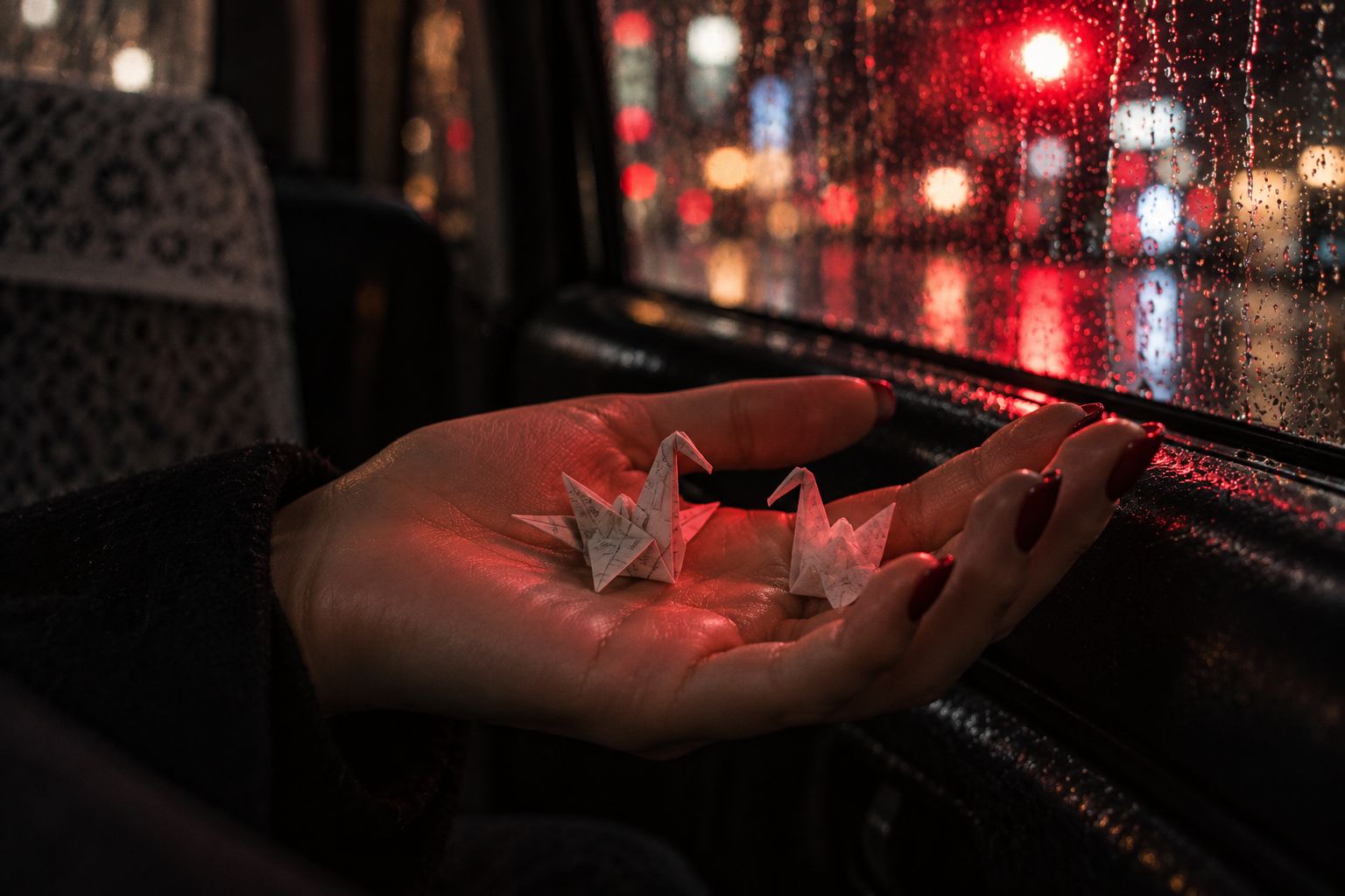 Zwei Papierkraniche auf Yamis Handfläche im roten Licht einer Ampel
